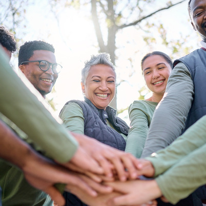 Teamwork, motivation and huddle with senior friends hiking together in the forest or woods from bel.